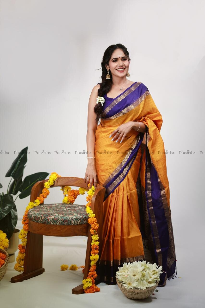 Woman wearing an orange saree with a purple and zari border