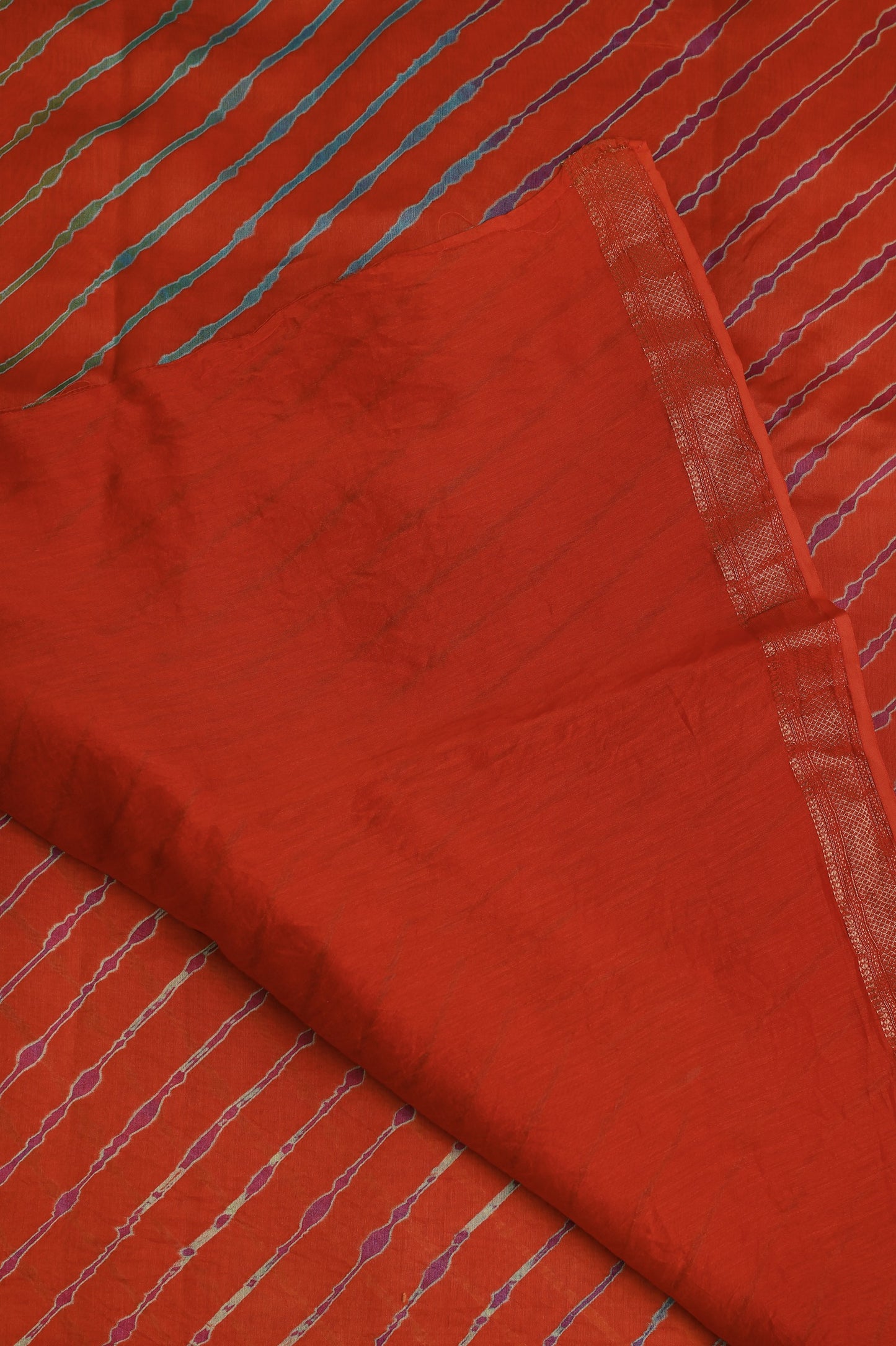 Orange-red saree with multicoloured diagonal Lahariya stripes and a narrow metallic border