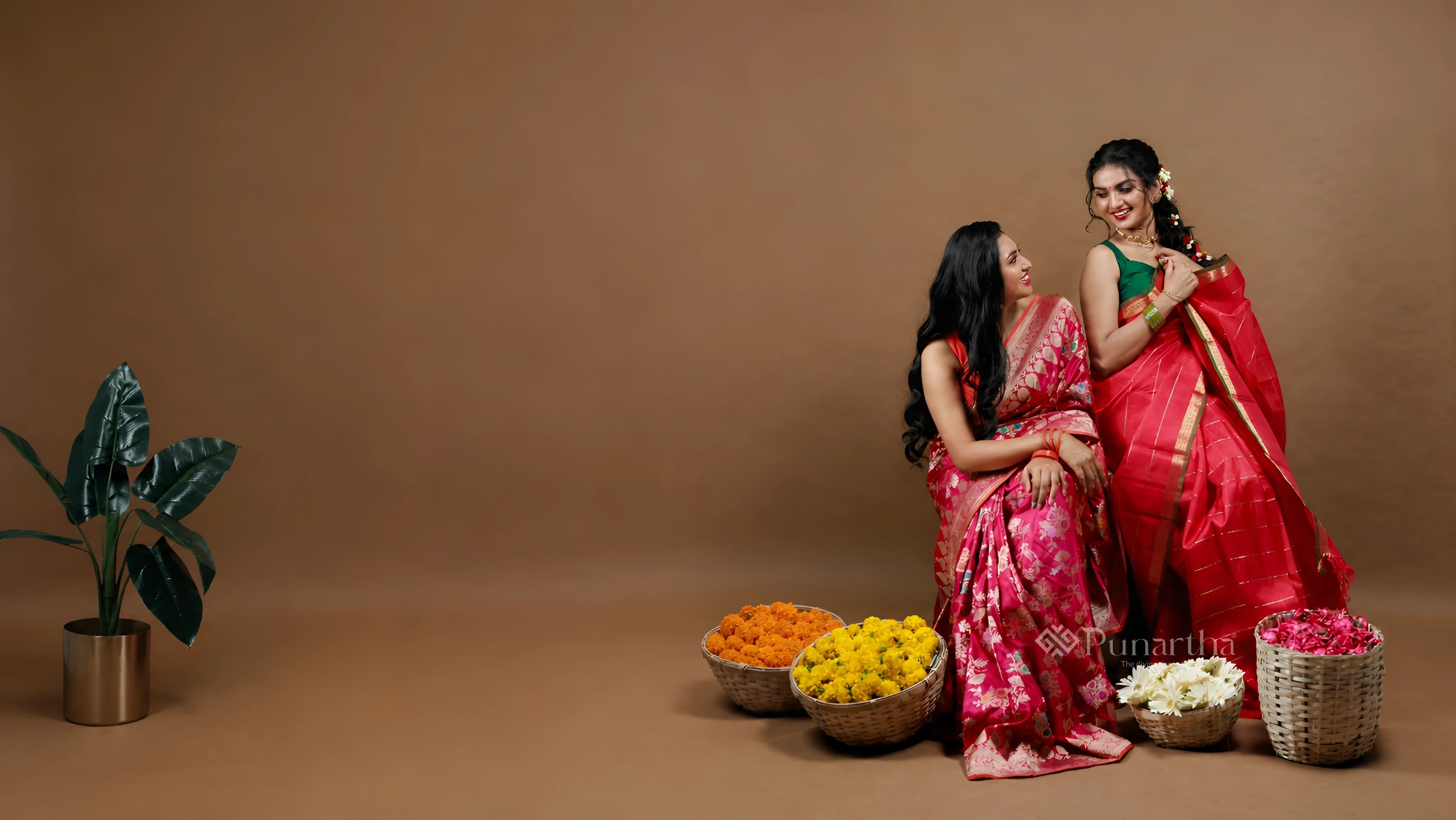 Two women sharing a warm moment in pink and red handwoven sarees