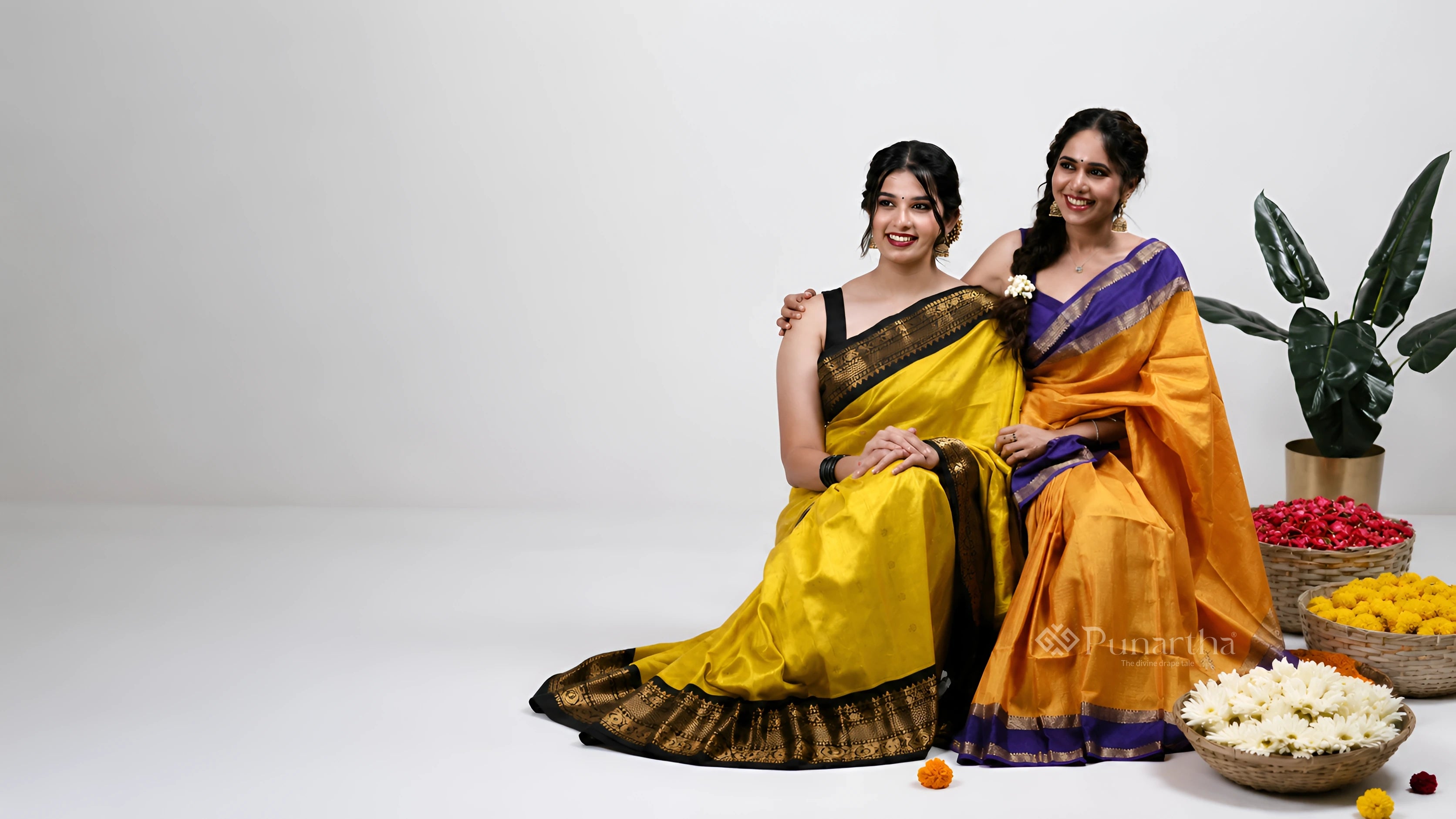 Two women seated together in yellow and orange silk sarees