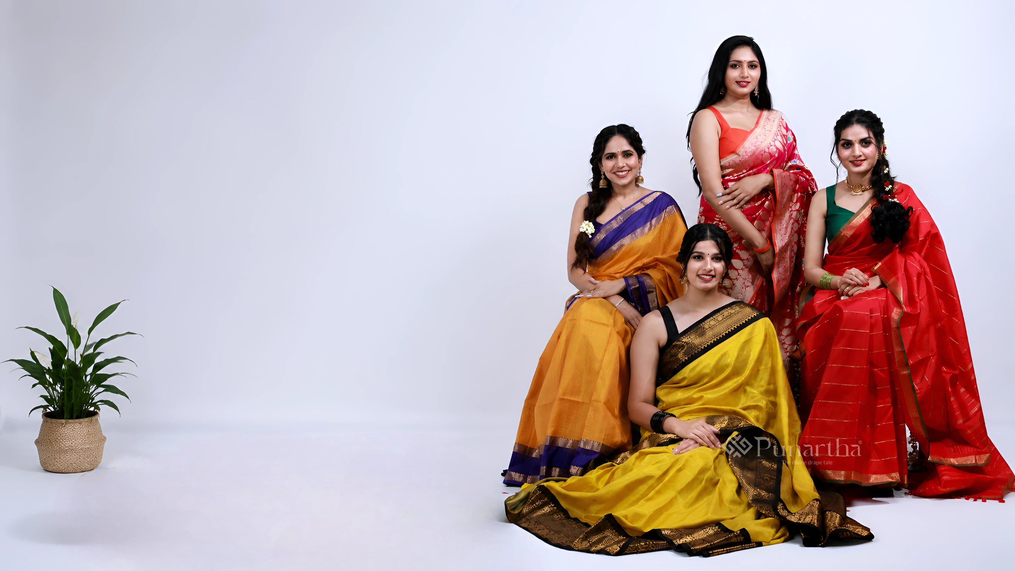 Four women posed in yellow, orange, pink and red silk sarees