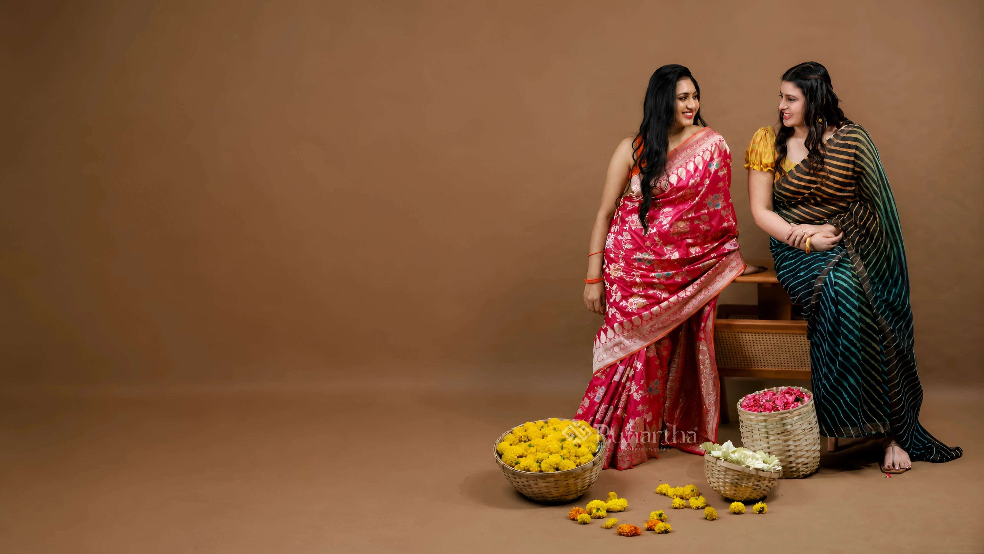 Two women in pink and black sarees sharing a conversation